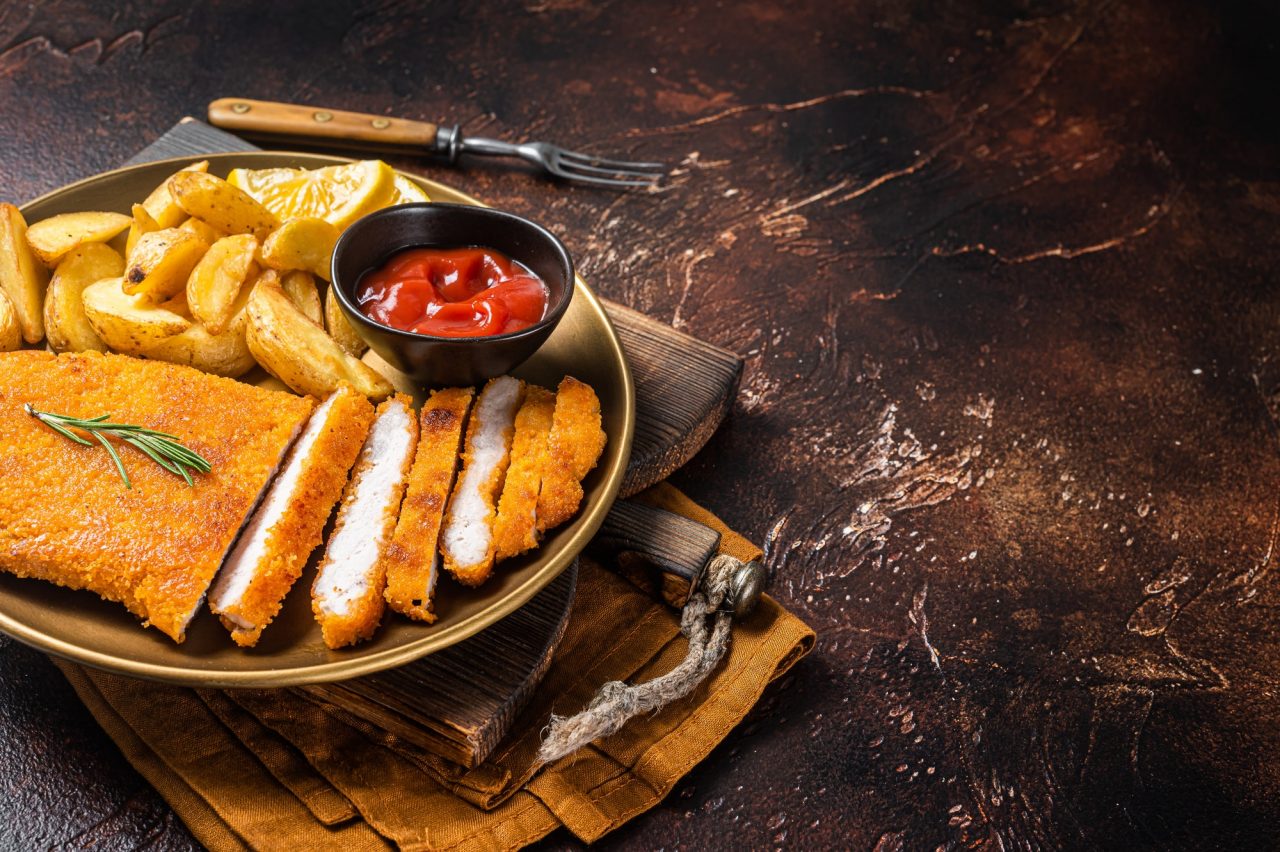 Breaded german weiner schnitzel with potato wedges. Dark background. Top view. Copy space